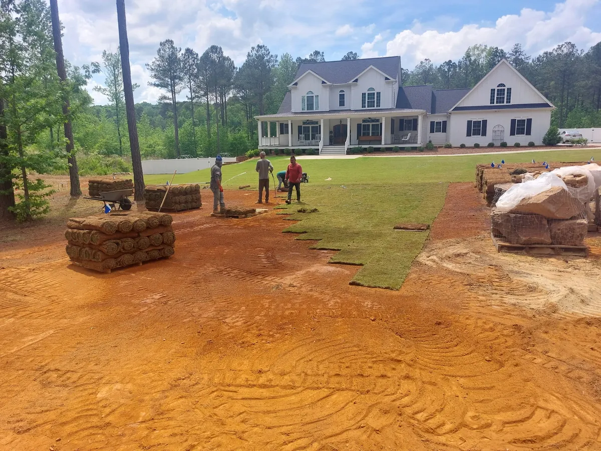 Georgia's Best Property Masters crew on a job site with pallets of fresh sod in front of a farmhouse