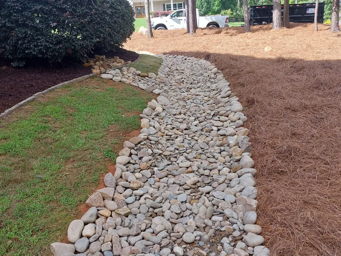 Dry creek bed of river rock winding through a pine straw bed beside a lawn