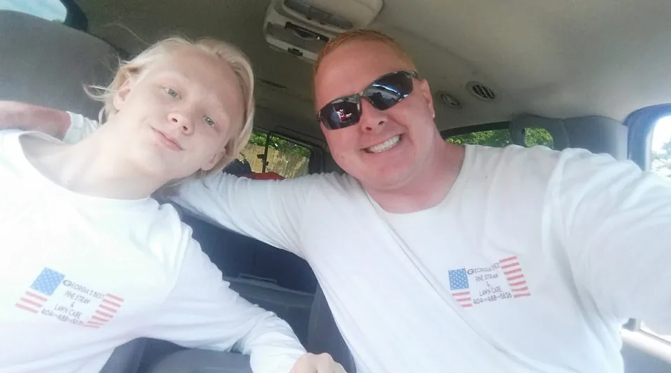 Hunter Henderson and his father, Brandon Henderson, smiling side by side in a truck in matching Georgia's Best work shirts
